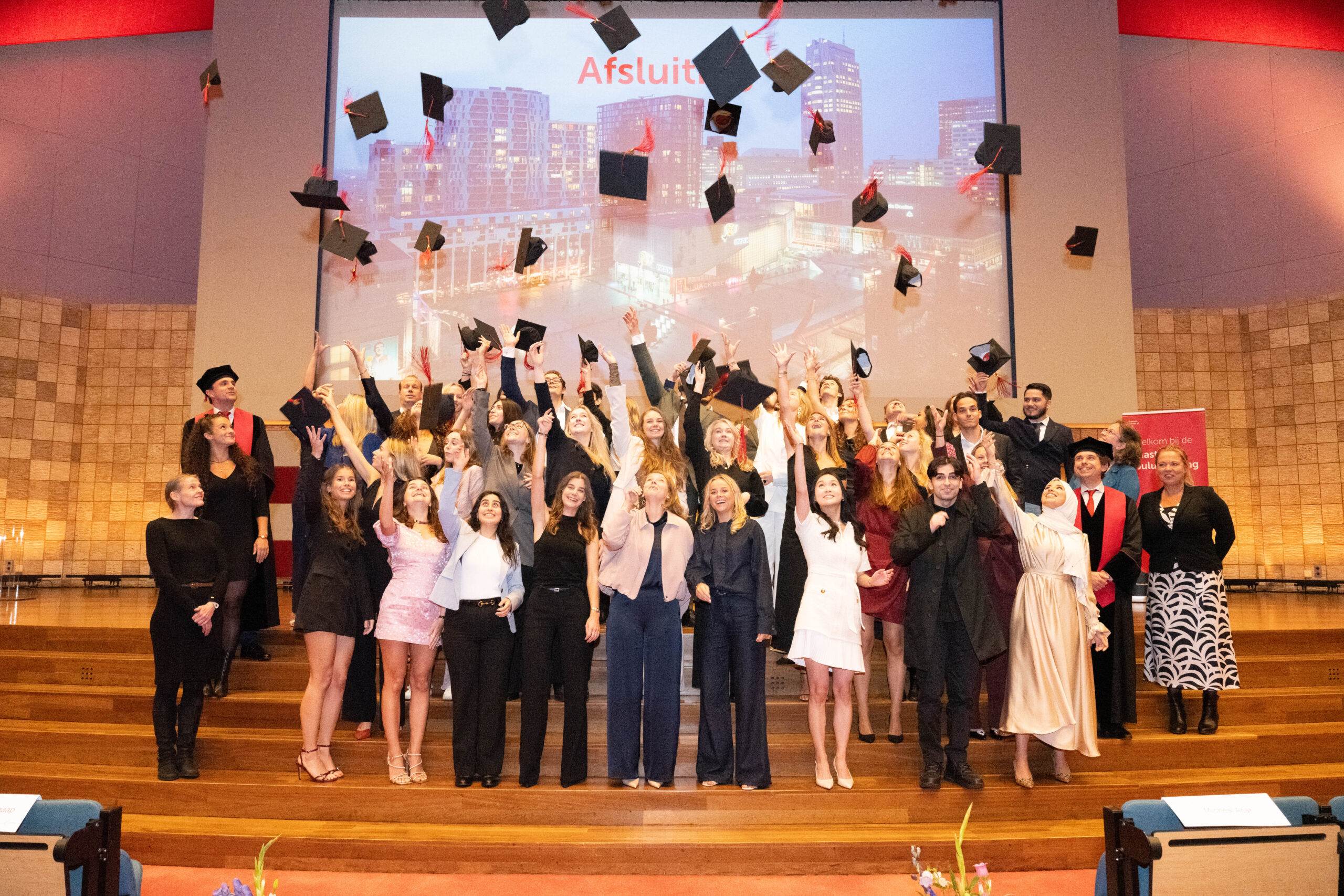 Een groep studenten gooit hun caps de lucht in.