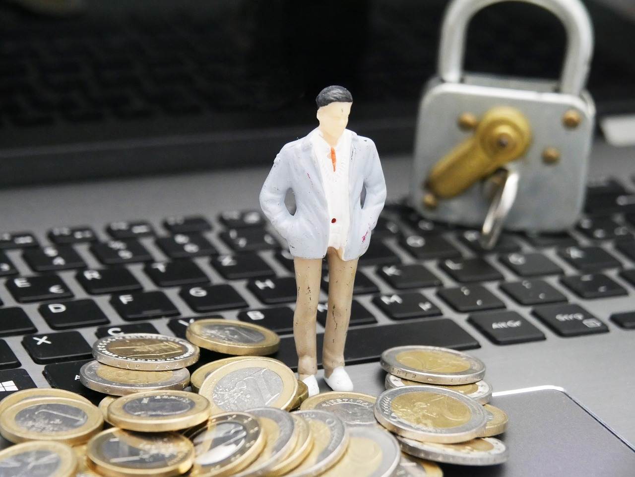 Een miniatuur poppetje staand tussen muntgeld op het toetsenbord deel van een laptop.